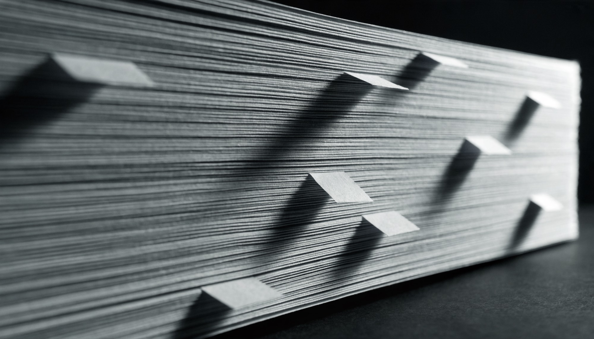 The compressed edge of a tall stack of printed paper, with plain tabs protruding at intervals.